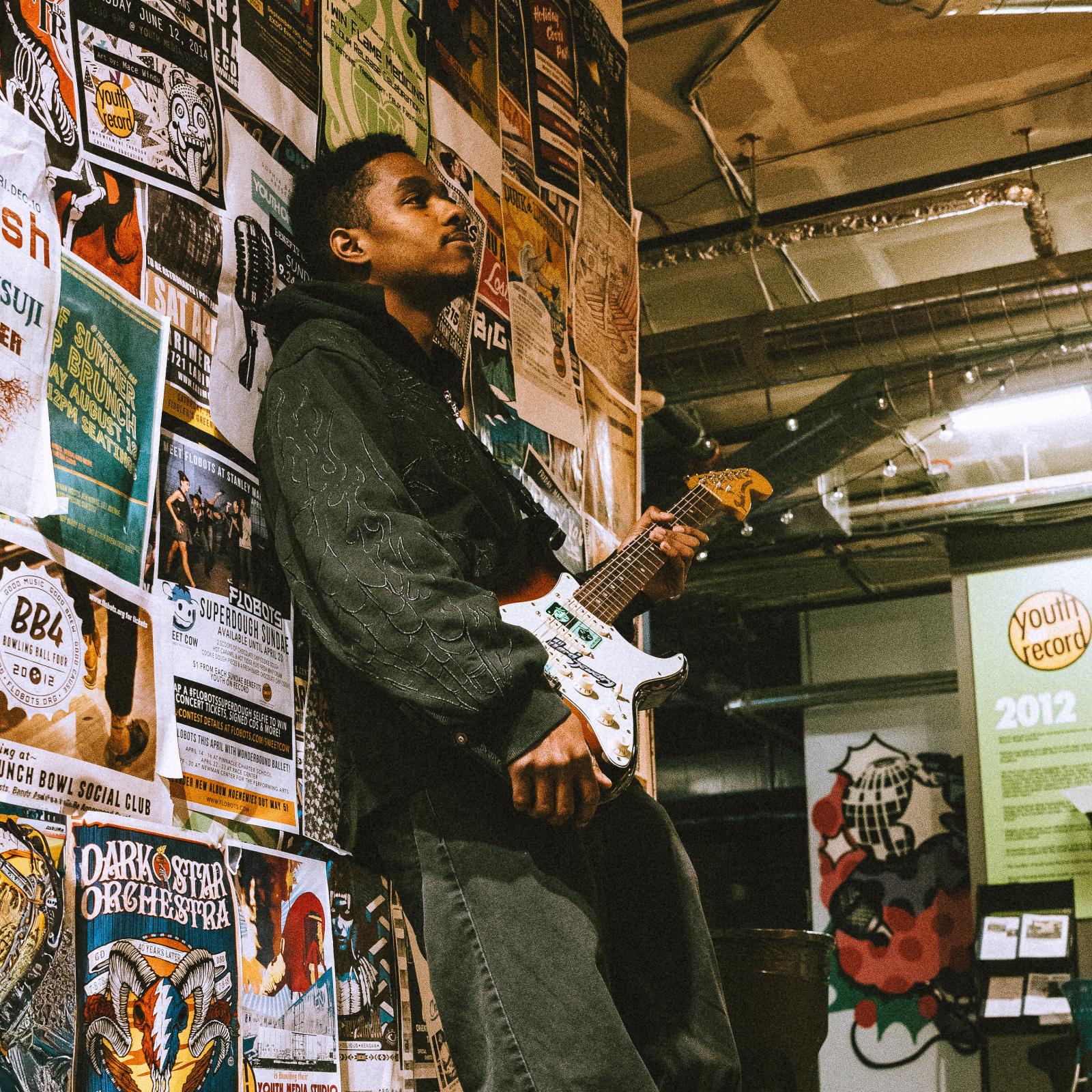 wulfsun holding guitar leaning against the wall 