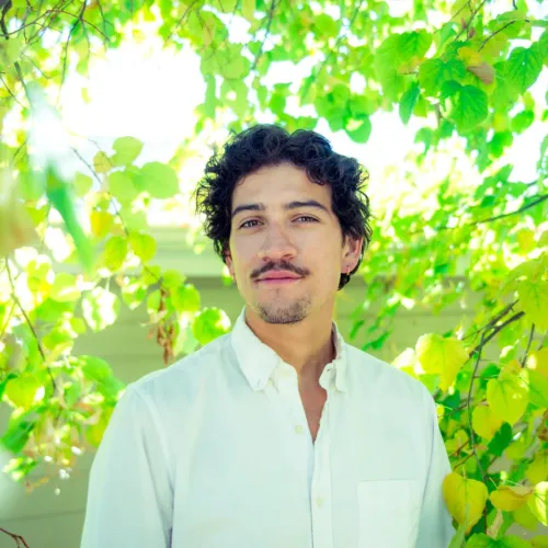 Conrad mata standing surrounded by bright green leaves of a tree