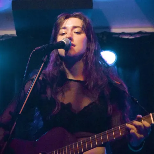 Genevieve performing on stage, playing guitar and singing into a microphone.