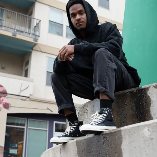 Wulfsun sits on concrete steps wearing black pants and a black hoodie